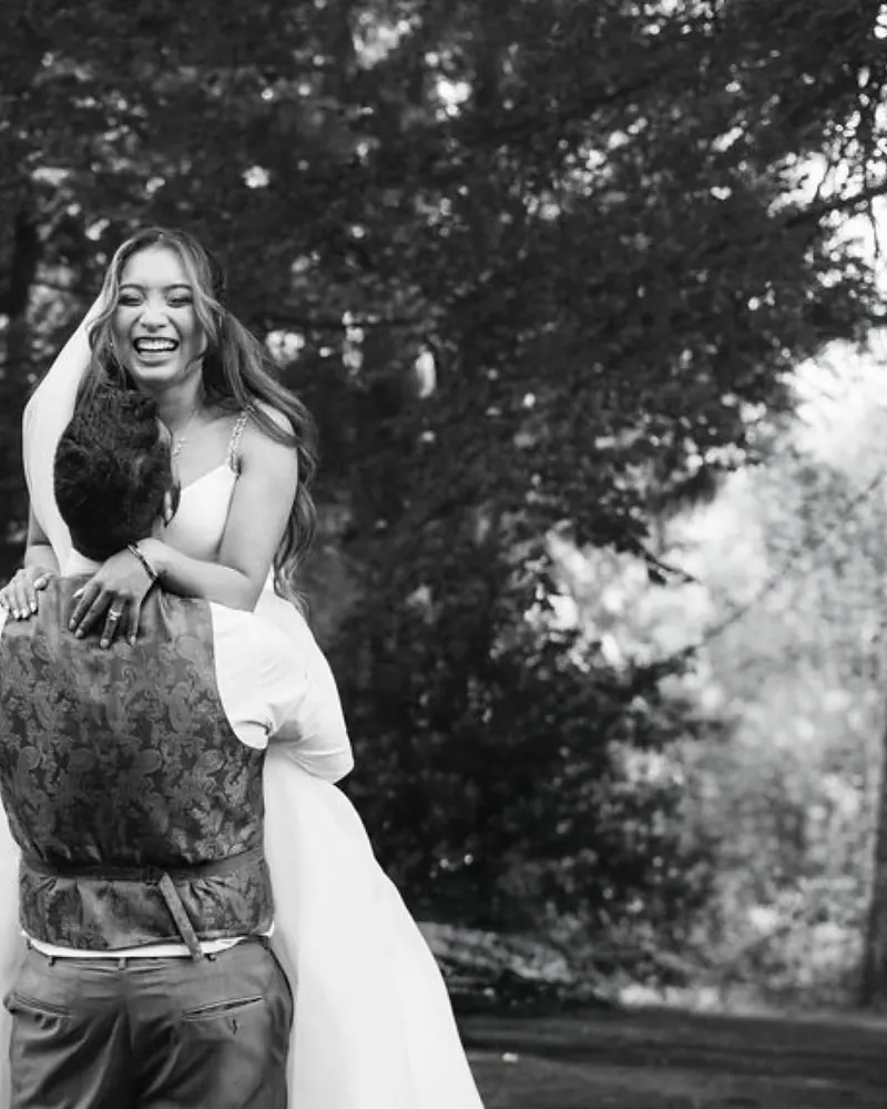 Black-and-white portrait of a bride laughing as her partner lifts her
