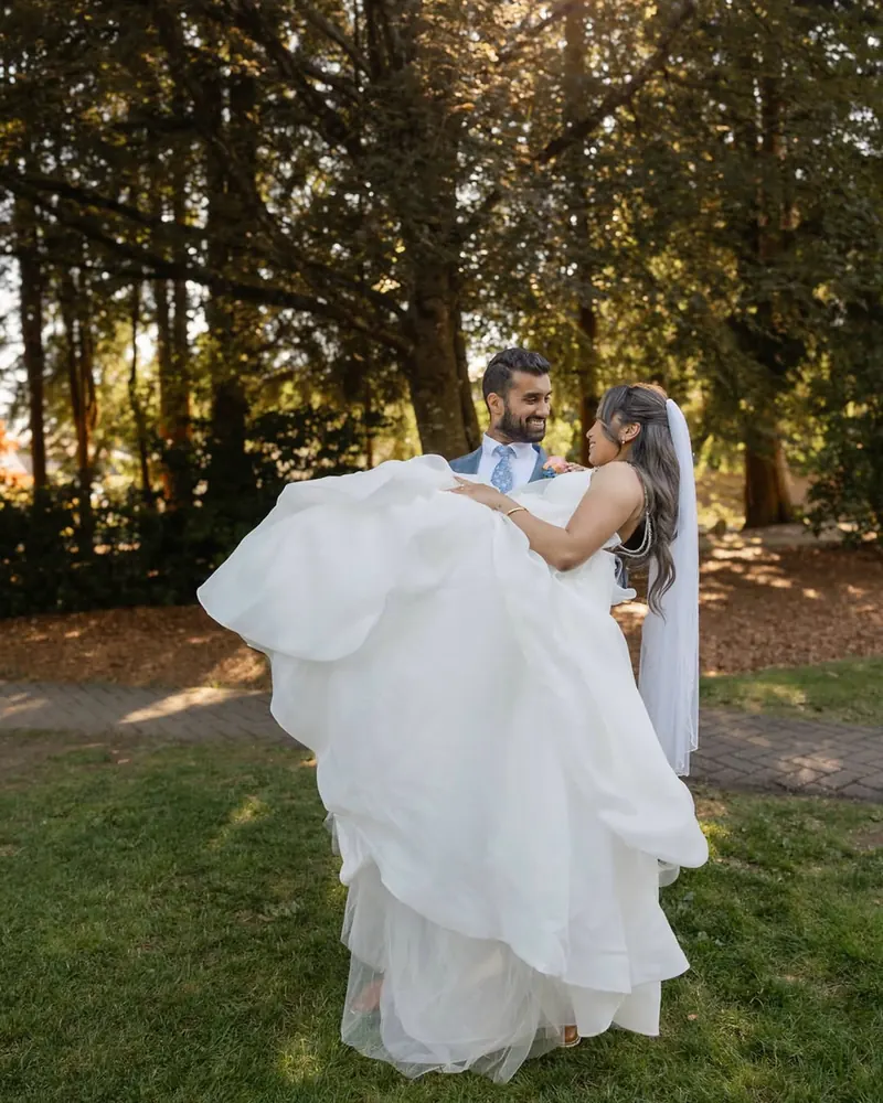A groom lifts his bride on a sunlit lawn