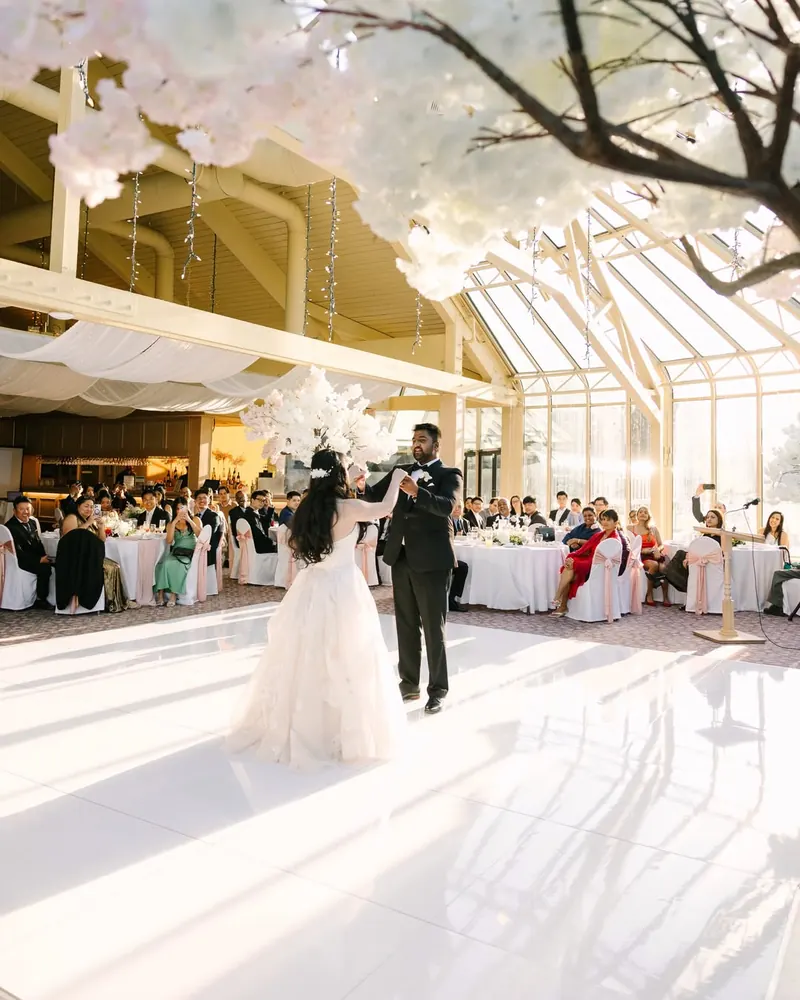 A couple’s first dance in a sunlit conservatory reception with blossom trees